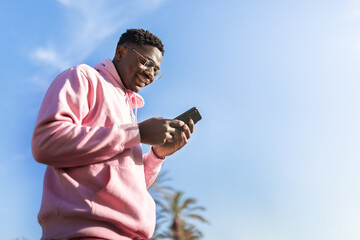 Low angle view of African American man using smart phone outdoors. Copy space