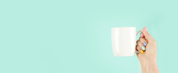 Arms raised up holding tea cup on green background.