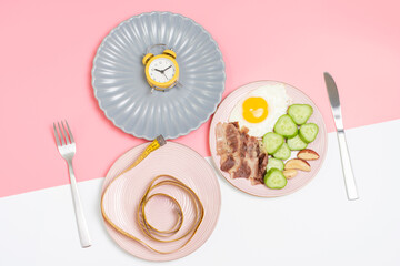 Plates with food, alarm clock and measuring tape top view on pink and white background, intermittent fasting concept.