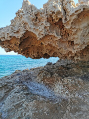 A stone, a rock, a hanging piece of long-frozen lava, below dried salt, similar to ice, against the background of the sea and a blue cloudless sky.