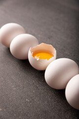 White chicken eggs and egg yolk in a row on black stone table. Very popular nutritious and economic food product. Concept image. Closeup view.