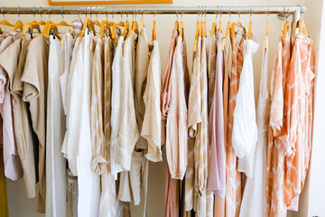 peach pastel colorful summer collection of natural clothes on hangers in retail fashion shop.