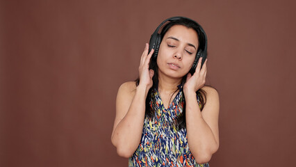 Indian woman having fun listening to music on headphones, using mp3 radio to enjoy audio song. Dancing on sound rhythm and melody for entertainment and leisure activity on camera.