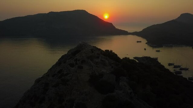 Golden orange sunset aerial orbits rocky peak on Mediterranean island