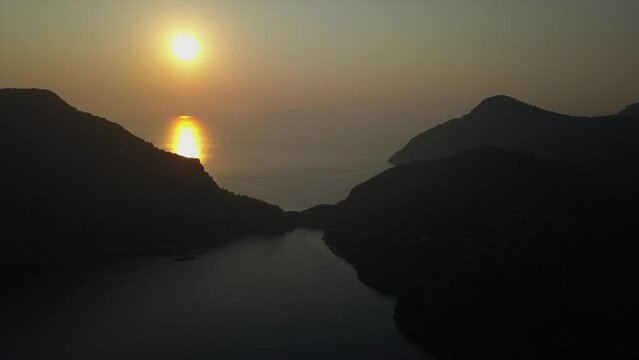 Aerial rises to reveal golden sunset beam on ocean water in dark dusk