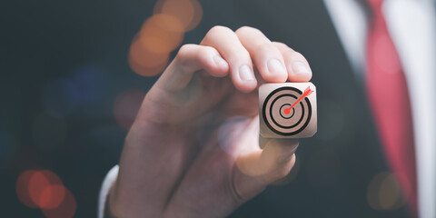 Wooden block in businessman hand and arrow icon hitting center of dartboard target,Setting business goals and focused concepts, Organizational growth and objectives, marketing strategy planning