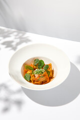 Tradition italian stuffed pasta - tortellini with minced meat. Italian ravioli on white background with harsh shadows. Summer menu italian restaurant. Tortellini with beef and spinach leaves