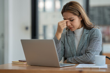 Beautiful asian businesswoman he adacheand stressed working in finance, management, marketing from laptop computer displaying revenue data on real estate projects in office interior.