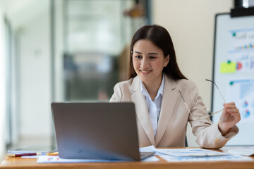 Attractive asian businesswoman holding eyeglasses working with financial, management, marketing data from laptop computer showing revenue data in growing real estate projects.