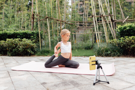 Sporty fit active caucasian girl in sportswear stretch sit legs split on mat outdoor at summer day. healthy kid do sport gymnastics workout exercise fitness training