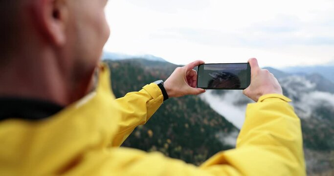 Male blogger tourist takes pictures of mountains and forest valley on phone