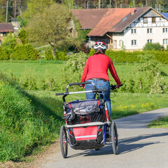 Junge Mutter unterwegs in idyllischer Natur mit Pedelec und Buggy.