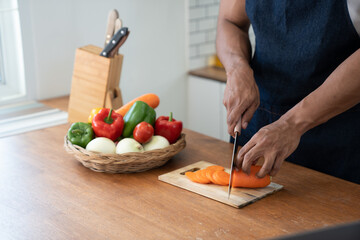 Asian strong man Wearing an apron having fun while preparing ingredients such as fruits and vegetables. learn how to do Chopping Carrots via Application Happily online in the kitchen.