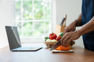 Asian strong man Wearing an apron having fun while preparing ingredients such as fruits and vegetables. learn how to do Chopping Carrots via Application Happily online in the kitchen.