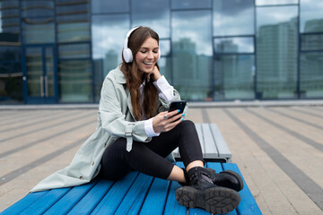 Fototapeta na wymiar female freelancer listening to music on headphones and chatting via video call using phone outside