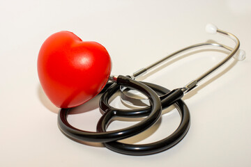 Selective focus of stethoscope on white surface with a red heart, medical concept