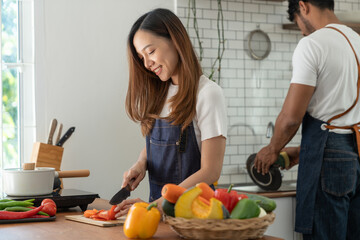 Image of Asian couple doing activities together by cooking learning how to do it online happily with healthy vegetable ingredients in their own homes, people-to-people concept and online education.