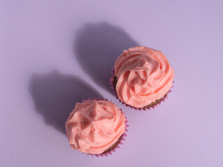 Delicious cupcakes with a lush pink cream cap, hard shadows, top view