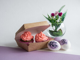 Delicious cupcakes with a lush pink cream hat in a box, take it with you, Easter painted eggs, flowers in a round glass vase, a place for text