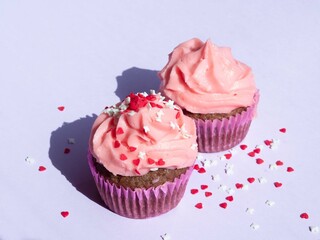 Delicious cupcakes with a lush pink cream cap on purple, sprinkled with confectionery sprinkles, hard shadows