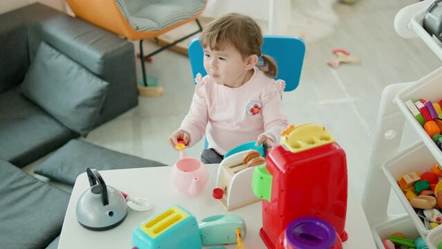 Girl Pretend Eating with Toy Spoon From Plastic Empty Bowl  in Kitchen Sitting by the Table at Home Playroom