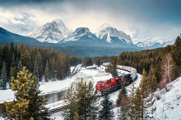 Morants Curve with iconic red cargo train passing through bow valley and rocky mountains in winter...