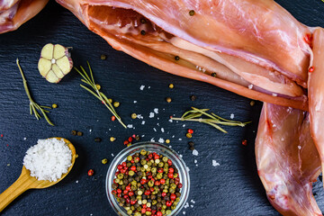 Rabbit meat with pepper, rosemary, salt and garlic on a slate board. Top view