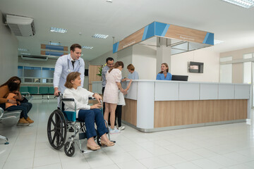 Doctor and nurse taking care and talking mature female patient sitting on wheelchair in hospital. Healthcare concept.
