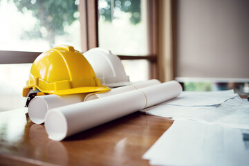 Yellow and white hard safety wear helmet hat placed on blueprint at construction site.