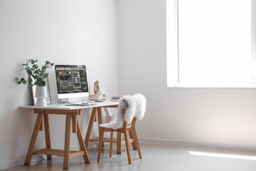 Modern workplace with computer and eucalyptus in vase near light wall