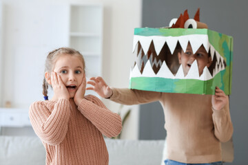 Scared little girl and her brother in cardboard dinosaur costume at home