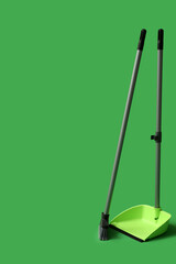 Dustpan with cleaning broom on green background