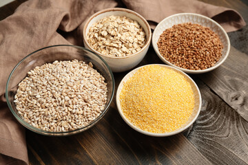 Bowls of different cereals on wooden table, closeup