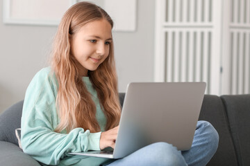 Fototapeta premium Little girl using laptop on sofa at home