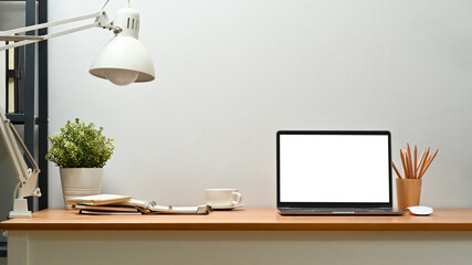 Front view of laptop, potted plant, lamp and supplies on wooden desk. Blank screen for text...