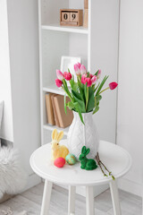 Vase with tulips, Easter eggs and rabbits on table in living room