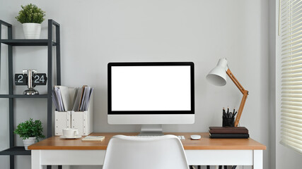 Front view of blank computer screen, lamp and supplies on wooden desk. Empty screen for your creative design