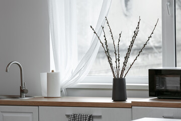 Vase with willow branches on counter near window in kitchen