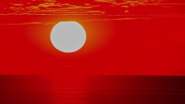 Bright red disk shape sun sets behind ocean horizon, fusion time lapse
