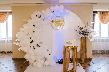 Arch decorated with a composition of white balloons, flowers and greenery in the hall. Golden...