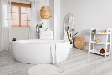 Interior of light bathroom with bathtub, shelving unit and mirror