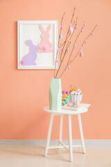 Vase with tree branches and Easter eggs on table in room