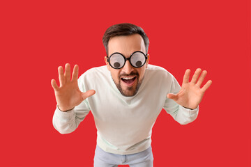 Fototapeta premium Angry young man in funny eyeglasses on red background. April Fools' Day celebration
