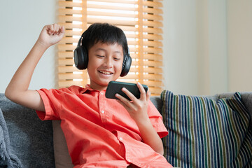 Excited Asian boy playing online game on smart phone with headphones.  - 573839029