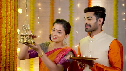 Happy young couple light up hanging lamp by holding diya plte during festival celebration at home - concept of diwali celebration, auspicious and indian culture
