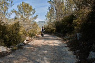 Fit male cyclist riding dirt trails on a gravel bike. A man riding a gravel bike on a gravel road in a scenic view with hills in Alicante region, Spain. Sports motivation.Gravel road in mountains.