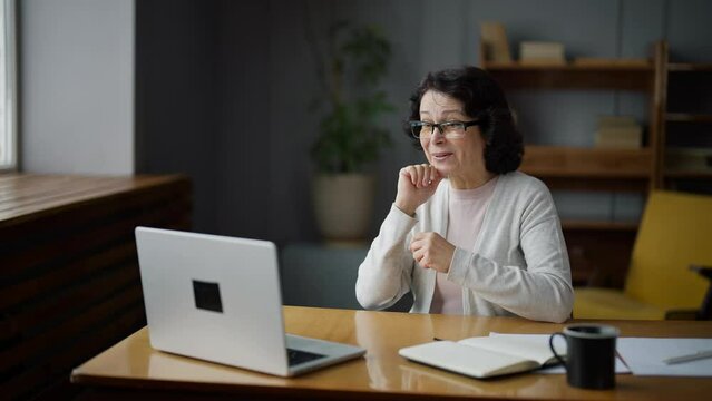 Happy woman smiling and waving hand, sitting in home and talking on video call using laptop camera. Online meeting with professional psychologist, freelance work, communication with beloved relatives.