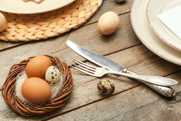 Nest with Easter eggs and cutlery on wooden background