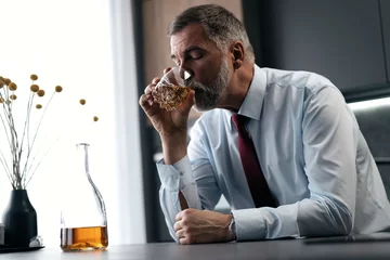 Fotobehang Relaxing after a hard working day. Confident mature businessman sitting at the table and drinking whiskey. © opolja