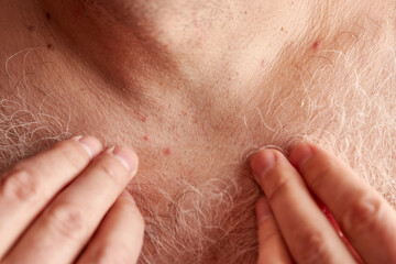 A man shaves the long gray hair on his chest.